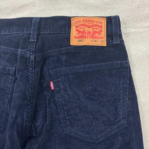 Può includere: Primo piano di jeans Levi's 505 in velluto a coste blu navy. La tasca posteriore e l'etichetta Levi Strauss & Co. sono visibili. L'etichetta recita "505" e "W 30 L 32". I jeans hanno un classico design a cinque tasche.