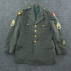 May include: An olive drab military dress jacket featuring gold-toned buttons, four front pockets with flaps, and shoulder epaulets. The sleeves and shoulders display embroidered patches and rank insignia, including chevrons and unit emblems.