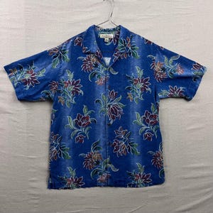 以下が含まれることがあります： 青色の半袖シャツ、花柄。 シャツはクラシックな襟、胸ポケット1つ、マルーンと白の花と緑の葉の鮮やかなプリントが特徴です。