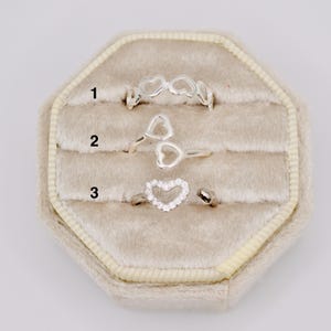 May include: Three silver-toned rings labeled 1, 2, and 3. Ring 1 features a continuous band of connected heart outlines. Ring 2 is an open-style band with two heart shapes. Ring 3 is an open band with a single heart outline encrusted with clear stones.