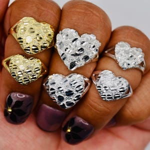 May include: A collection of five heart-shaped rings featuring a textured, nugget-style surface. Two rings are finished in a bright yellow gold tone, while three rings are finished in a polished silver tone, each with a smooth, thin metal band.