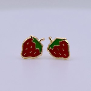 May include: A pair of strawberry-shaped stud earrings. Each earring features a red body with small white seeds, a green leaf, and a gold-colored border. The earrings are designed to be worn on the earlobes.