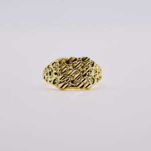 May include: A yellow gold ring featuring a textured nugget-style design across the top surface. The metal surface displays a combination of irregular, raised bumps and recessed, diagonal line patterns that create a reflective, multi-faceted appearance.
