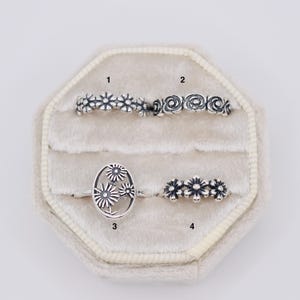 May include: Four silver rings labeled 1 through 4. Ring 1 features a daisy chain pattern. Ring 2 has a repeating rose motif. Ring 3 is an oval shape with three daisy flowers. Ring 4 displays a horizontal row of three small daisy flowers.