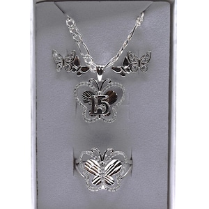 May include: A silver-toned jewelry set featuring a butterfly theme. The set includes a necklace with a pendant, a pair of earrings, and a ring. The pendant and ring feature the number "15". The jewelry is set in a gray box.