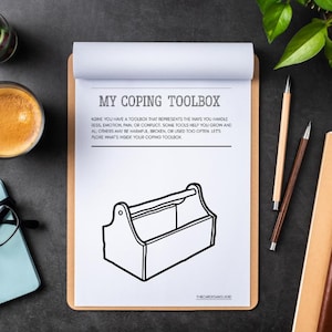 May include: A clipboard with the text "MY COPING TOOLBOX" and a line drawing of a toolbox. The image includes a cup of coffee, pencils, glasses, and a plant on a dark surface.