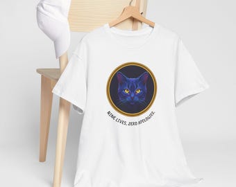 May include: White t-shirt featuring a blue cat illustration within a gold circular frame. The cat has yellow eyes and is set against a dark background. The text "NINE LIVES, ZERO APOLOGIES" is printed below the graphic.