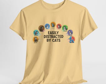 May include: A light yellow t-shirt with the text "EASILY DISTRACTED BY CATS" in black. The shirt features a colorful design of cat illustrations in a rainbow arc.