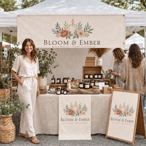 Può includere: Uno stand di mercato per Bloom & Ember con un banner bianco, un tavolo con candele di soia in barattoli di vetro e un cartello in legno. Il marchio presenta un'illustrazione di una candela e fiori con il testo Bloom & Ember.