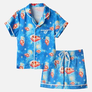 Op de afbeelding: Blauwe pyjamaset met een pizza- en hemels patroon. De top met korte mouwen en de shorts hebben witte biezen en een taille met trekkoord. De pizzapunten zijn rood, wit en geel. De achtergrond heeft een sterrenhemel met manen.
