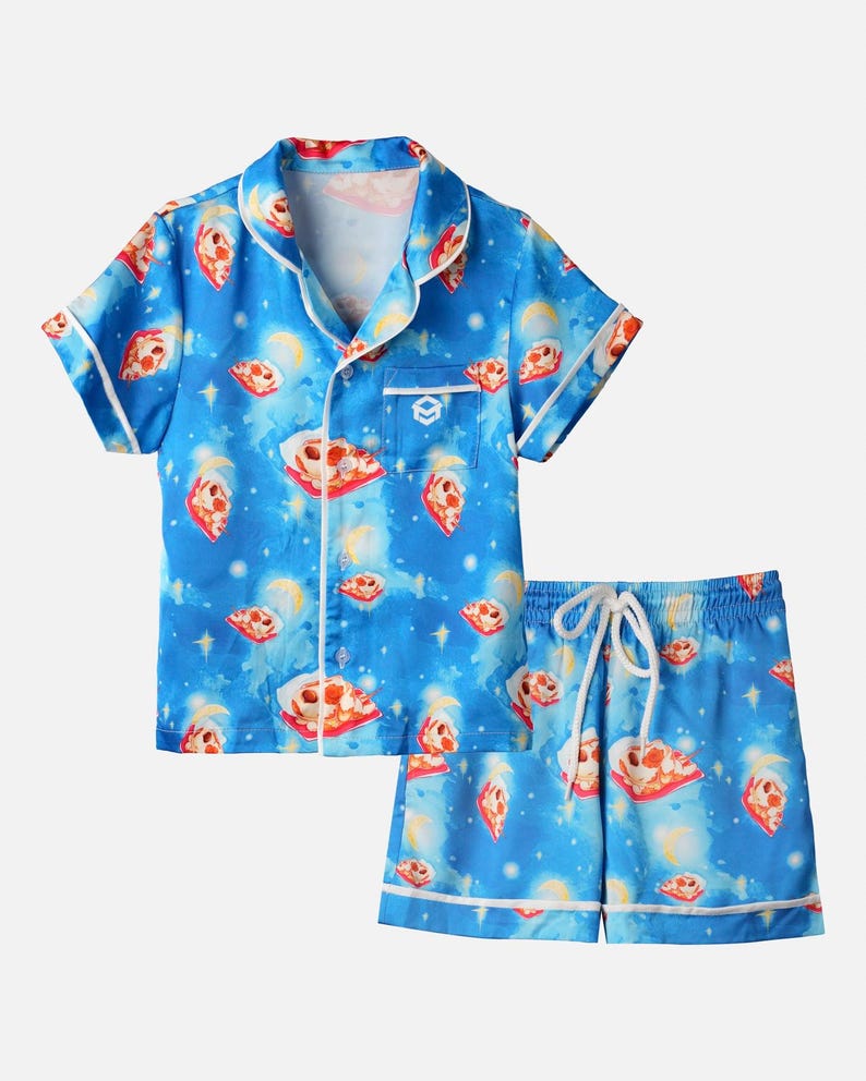 Op de afbeelding: Blauwe pyjamaset met een pizza- en hemels patroon. De top met korte mouwen en de shorts hebben witte biezen en een taille met trekkoord. De pizzapunten zijn rood, wit en geel. De achtergrond heeft een sterrenhemel met manen.