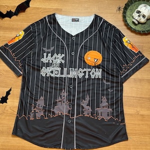 May include: Black baseball jersey with white vertical stripes, featuring the text "Jack Skellington" and a pumpkin design. The jersey has a button-up front and short sleeves. The design includes bats and haunted houses.