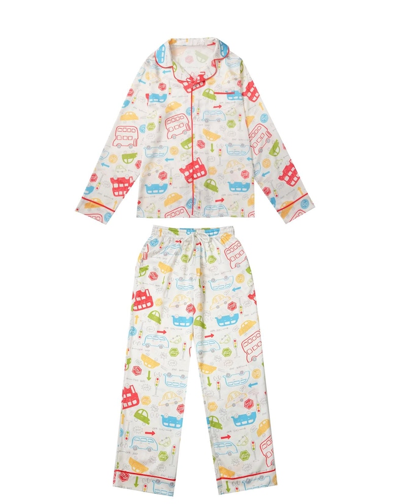 Op de afbeelding: Witte pyjamaset met een kleurrijk autopatroon. De top met lange mouwen en de broek hebben een herhalend ontwerp van bussen, auto's en verkeerslichten in rood, blauw, groen en geel. De set heeft rode biezen en een taille met trekkoord.