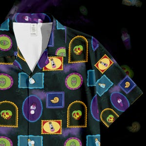 May include: Dark green button-up shirt with a repeating pattern of colorful, framed illustrations. The illustrations include skulls, potion bottles, and alien-like faces. The shirt has a V-neck collar and short sleeves.