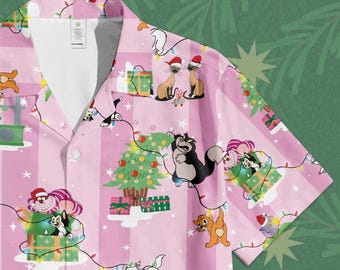 May include: Pink button-up shirt with a Christmas-themed cat print. The shirt features a repeating pattern of cartoon cats, Christmas trees, and wrapped gifts. The cats are wearing Santa hats and are surrounded by string lights. The background has vertical stripes.