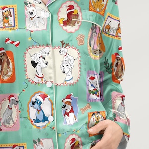 Op de afbeelding: Lichtgroene pyjamatop met een herhalend patroon van cartoonhonden in kerstmutsen en kaders. De pyjamatop heeft witte biezen en knopen. De afbeelding toont een close-up van de pyjamatop.