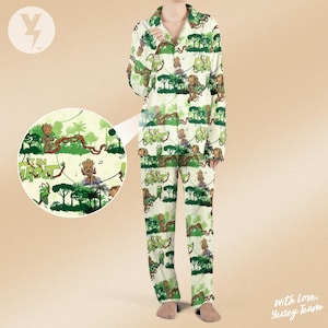 May include: Cream-colored pajama set featuring a repeating pattern of a cartoon character, trees, and the text "I AM GROOT" in green. The long-sleeved top has a button-down front and the pants have a relaxed fit. The set is made of a soft, lightweight fabric.