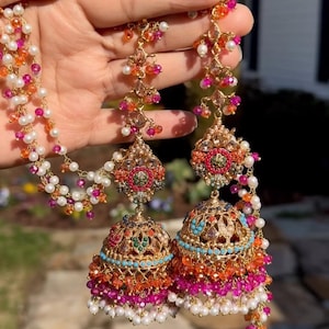 May include: A pair of gold-tone jhumka earrings featuring intricate metalwork, accented with multi-colored beads in shades of pink, orange, turquoise, and white. The earrings include long, dangling chains adorned with matching beads and pearls.
