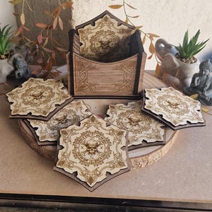Op de afbeelding: Een set van zes houten onderzetters met een houder. Elke onderzetter heeft een lasergesneden ontwerp van een schedel in een decoratieve rand. De onderzetters zijn zeshoekig en gemaakt van lichtbruin hout.