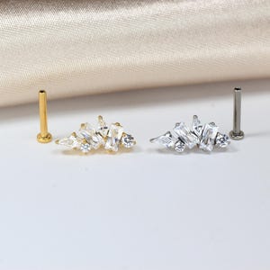 May include: Two flat-back earrings with a cluster of clear, rectangular and round-cut crystals. One earring is gold-toned, the other is silver-toned. A gold and silver post are also visible. Jewelry.