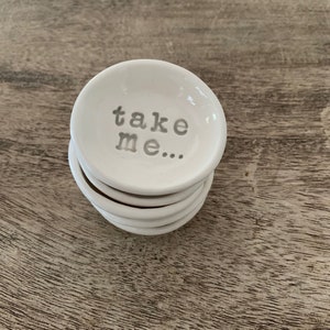 May include: A stack of white ceramic ring dishes with the words "take me..." embossed on the top dish.