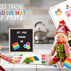 May include: A Christmas elf doll sits on a table with a colourful fidget toy. The elf is wearing a red hat with white trim, a green shirt with red and white stripes, and red trousers with white stripes. The elf is holding a rainbow pop-it fidget toy. The table has a sign that says "Get Your Trading On!" and a trading mat with a Christmas tree, a rainbow pop-it, and other fidget toys.