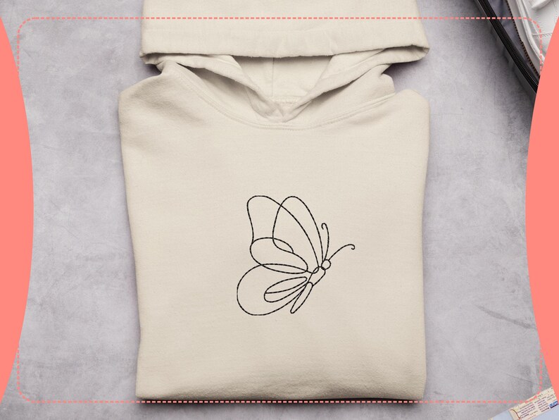 May include: A cream-colored hoodie with a black line drawing of a butterfly on the front. The butterfly design is minimalist, with a single continuous line forming the wings and body. The hoodie has a hood and a kangaroo pocket.
