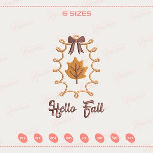 Op de afbeelding: Een geborduurd ontwerp met een bruine strik, een gouden blad en de woorden "Hello Fall". Het ontwerp is ingesloten in een gouden, gedraaide lijst. De afbeelding staat tegen een lichte achtergrond met een perzikkleurige rand.