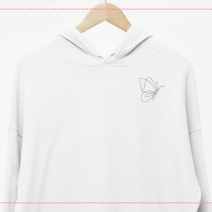 May include: White hoodie with a minimalist black butterfly outline design on the upper left chest. The hoodie is hanging on a wooden hanger against a white background. The butterfly design is a simple, continuous line.