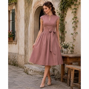 May include: A dusty rose midi dress featuring a stand collar with a small V-neck opening, short cap sleeves, and a fitted bodice. The dress includes a matching fabric tie belt at the waist and a full, pleated skirt that falls below the knees.