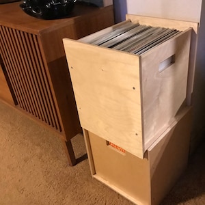 May include: Two stacked wooden record storage boxes. The top box is filled with vinyl records. The bottom box is empty.