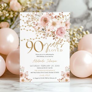 May include: A white birthday invitation card with gold lettering and floral decorations. The card announces a 90th birthday celebration, with the words "90 years loved". Features pink roses and decorative string lights.