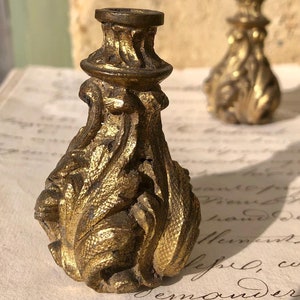 Könnte beinhalten: Zwei verzierte goldfarbene Möbelfüße mit einem detaillierten floralen Design.