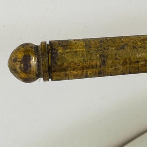 Puede incluir: Primer plano de una varilla de latón vintage con un extremo redondeado. La varilla tiene una superficie texturizada y un aspecto ligeramente deslustrado, lo que sugiere antigüedad. El latón tiene un tono dorado cálido y la varilla parece ser un componente de un artículo más grande.