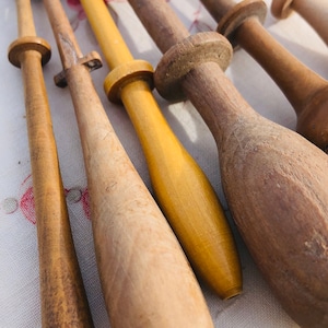 Può includere: Una collezione di bobine di legno per la creazione di pizzi. Le bobine sono di varie tonalità di marrone e giallo, alcune hanno una finitura liscia e altre una finitura più strutturata.