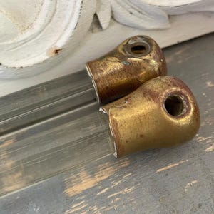 以下が含まれることがあります： 片端に古びた真鍮色の金属製キャップが付いた2本の透明なガラス棒。各金属製キャップには円形の開口部があり、緑青や摩耗の跡が見られ、滑らかで透明なガラス本体とは対照的な、風化した金属仕上げが施されています。