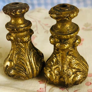 Könnte beinhalten: Zwei verzierte vergoldete Metall-Abschlüsse mit aufwendigen floralen Designs. Die Abschlüsse haben eine bauchige Form und eine glatte, polierte Oberfläche.