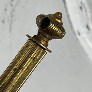 Könnte beinhalten: Nahaufnahme eines Vintage-Messingobjekts mit einem dekorativen, geriffelten Design. Das Objekt hat eine zylindrische Form mit einer kleinen, abgerundeten Oberseite und einem Loch. Das Messing hat eine warme, gealterte Patina, was darauf hindeutet, dass es sich um einen antiken oder Vintage-Artikel handelt.