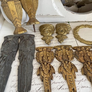 Könnte beinhalten: Eine Auswahl antiker dekorativer architektonischer Metallelemente in verschiedenen Formen und Größen. Die Teile sind in Gold- und Dunkelgrautönen gehalten und weisen verzierte Blumen- und geometrische Designs auf. Einige haben Schraubbefestigungen.