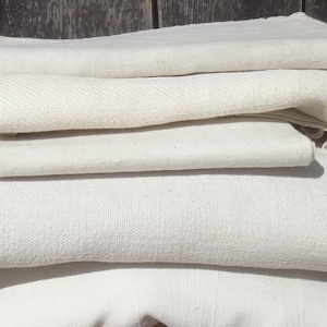 Può includere: Un mucchio di tessuto bianco, probabilmente lino, piegato con cura. Il tessuto ha una texture sottile e sembra essere di alta qualità.