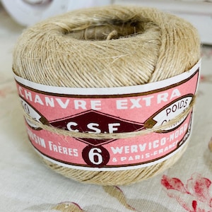 May include: A spool of natural twine with a pink and white label that reads "Chanvre Extra" and "C.S.F. Cousin Frères 6 Werivico-Nord Paris, France".