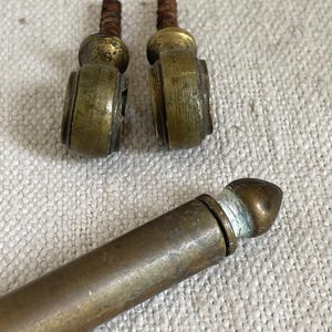 以下が含まれることがあります： 真鍮製のアンティーク家具金具3点。2つは小さく、ねじ付きのポストと装飾的な円筒形の本体が付いています。3つ目は、丸みを帯びた端を持つ、より長い円筒形のピースです。すべてのピースに経年劣化と摩耗の兆候が見られます。