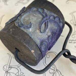 Pode incluir: Um rolo de madeira escura com um design floral decorativo azul e cinza. O rolo tem uma alça de metal e está sobre uma superfície estampada. O rolo é provavelmente usado para aplicar tinta ou tinta.