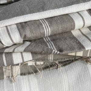 May include: A stack of striped fabric in shades of grey and white. The fabric is folded and layered, creating a textured and visually appealing pattern.