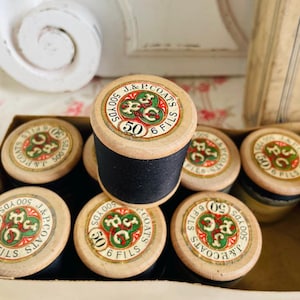 Pode incluir: Uma coleção de carretéis de linha vintage J. & P. Coats. Os carretéis de madeira têm um rótulo circular com o texto "J. & P. Coats 50 6 Fils 500 YDS". A linha é preta.