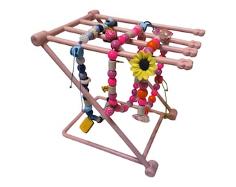 May include: A pink metal jewelry display stand holding several beaded necklaces. The necklaces feature various colors, including pink, blue, and orange, with decorative elements like a yellow sunflower. The stand has a geometric design.