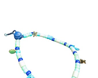 May include: A beaded bracelet with a nautical theme. The bracelet features a mix of blue, white, and green beads, with small gold starfish charms and a blue tassel. The bracelet is approximately 7 inches in length.