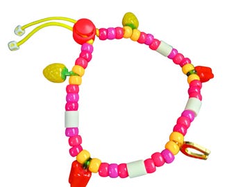May include: A colorful beaded bracelet with a playful design. The bracelet features pink, yellow, and white beads, with red and yellow fruit-shaped charms. It has a yellow elastic cord with white end pieces and a red clasp.