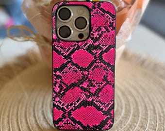 Puede incluir: Una funda de teléfono rosa intenso y negra con estampado de piel de serpiente. La funda tiene un borde negro y recortes para las lentes de la cámara del teléfono. La funda está diseñada para un teléfono inteligente.