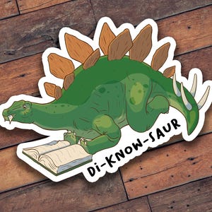 May include: A sticker featuring a green cartoon Stegosaurus reading a book. The dinosaur has brown plates on its back and white spikes on its tail. The text "Di-Know-Saur" is below the dinosaur.